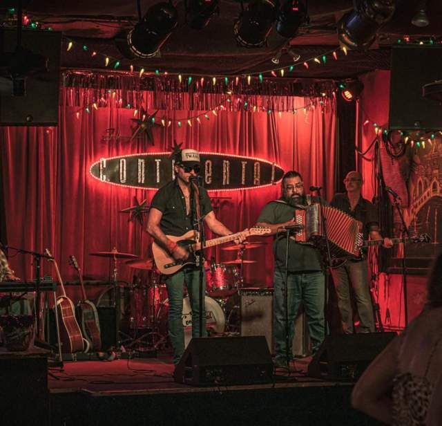 A live band performs on stage at the Continental Club under red lights.